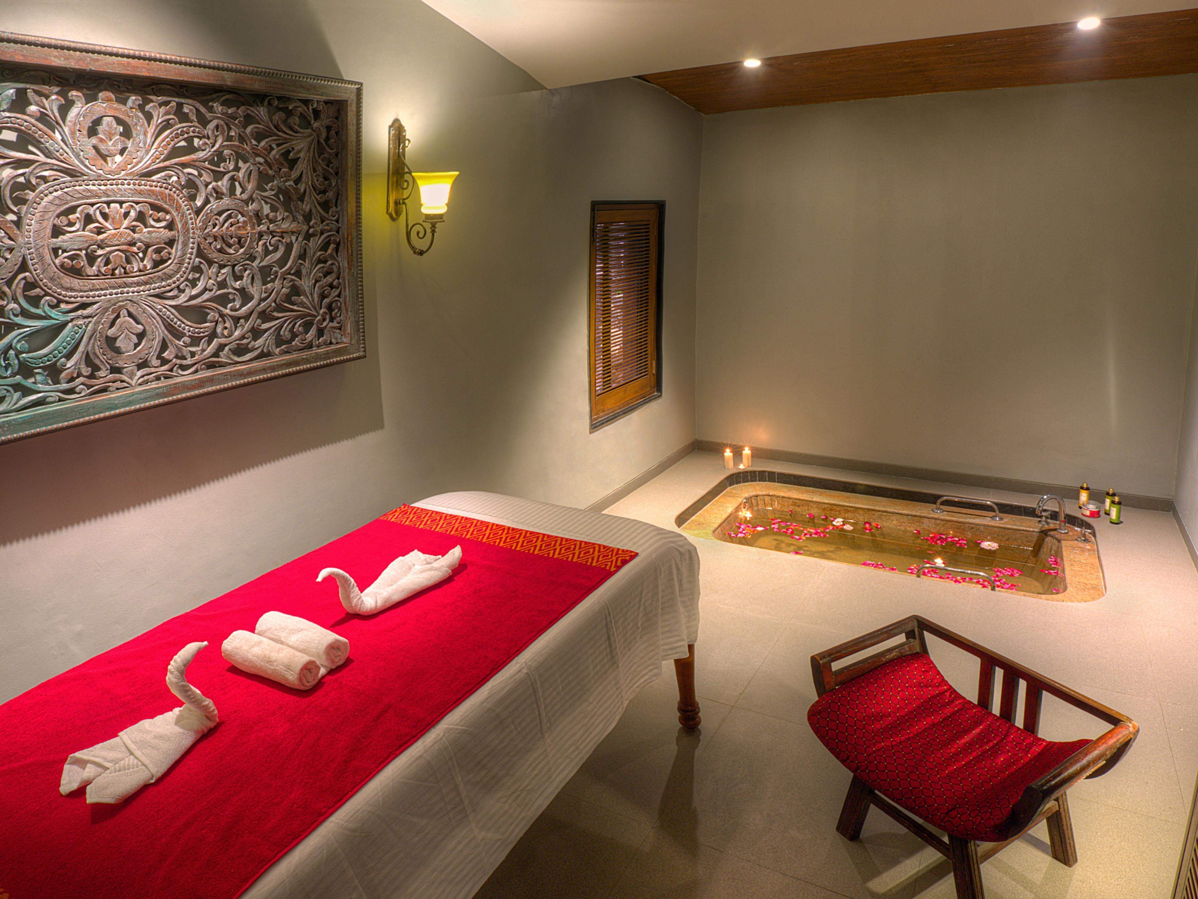 Luxurious spa room at Ramsukh Resort with a massage table and a rose-petal-filled hot tub.